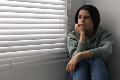 Photo of Sadness. Unhappy woman near window at home