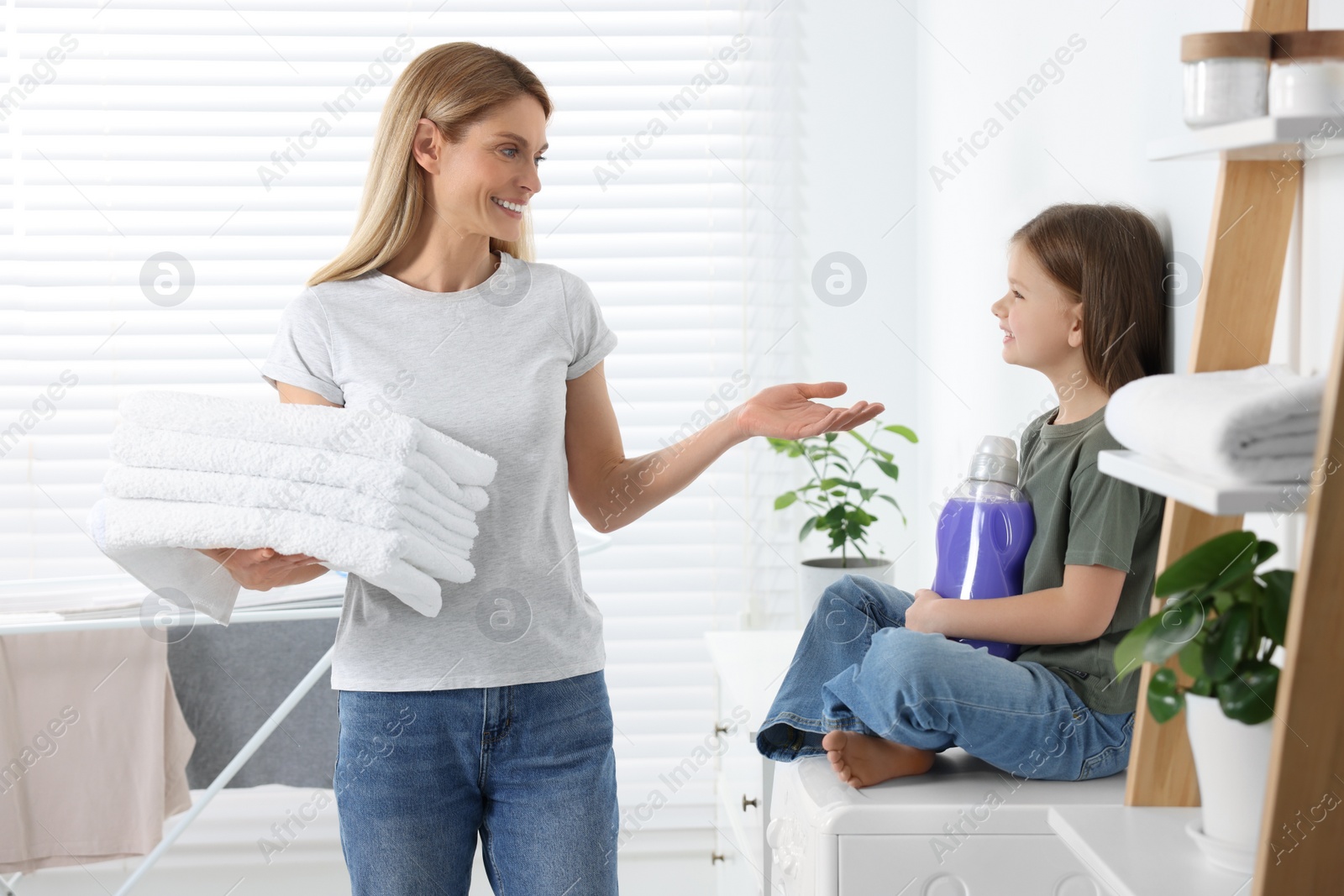 Photo of Mother and daughter holding clean towels and fabric softener in bathroom