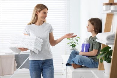 Mother and daughter holding clean towels and fabric softener in bathroom