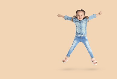 Cute girl jumping on beige background, space for text