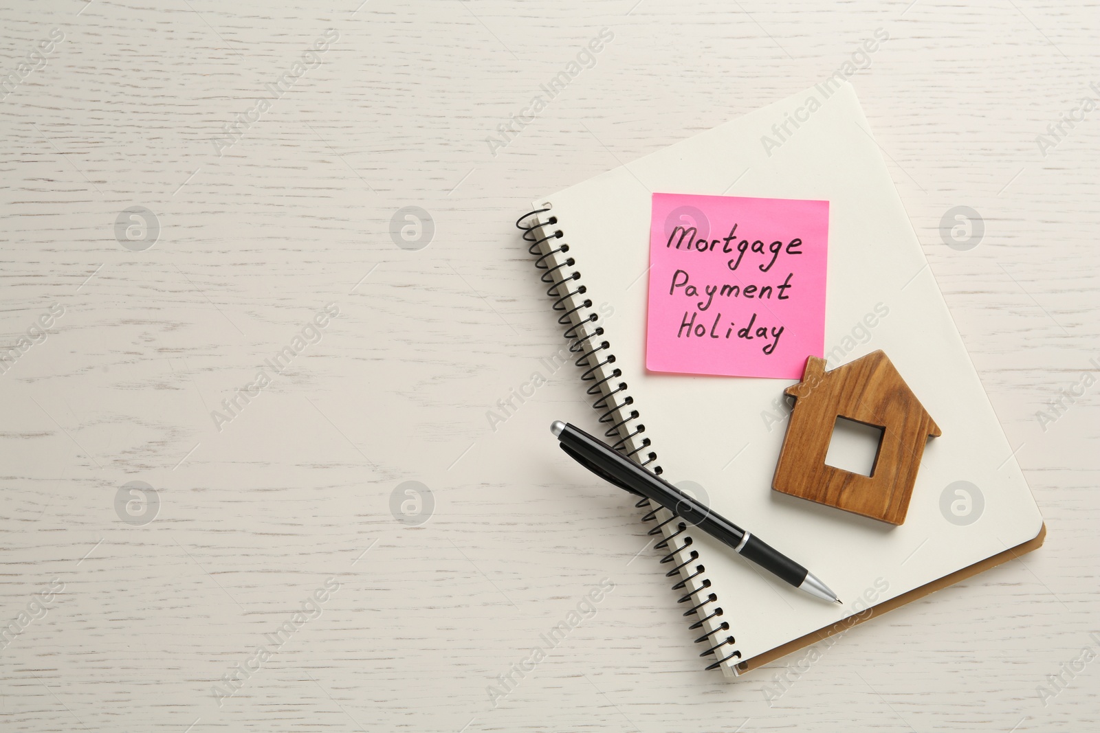 Photo of Paper note with words Mortgage Payment Holiday, notebook, pen and house model on white wooden table, top view. Space for text