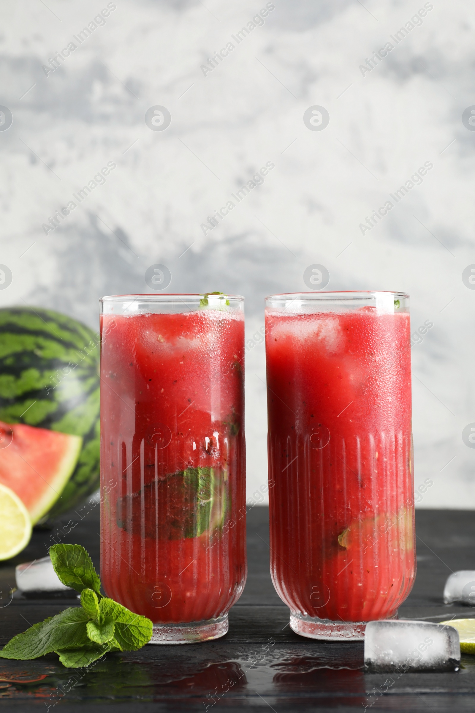 Photo of Glasses of delicious fresh watermelon juice, lime, mint and ice on black wooden table against textured wall. Space for text
