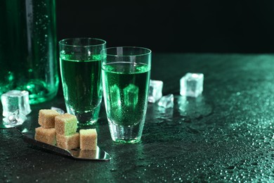 Photo of Absinthe in shot glasses, spoon, brown sugar and ice cubes on gray table, space for text. Alcoholic drink