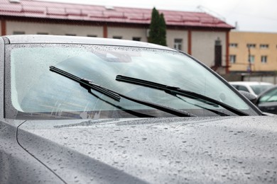 Car wipers cleaning water drops from windshield glass outdoors, closeup