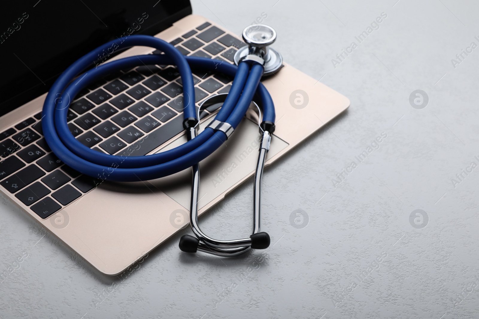 Photo of Laptop with stethoscope on white table, closeup. Space for text