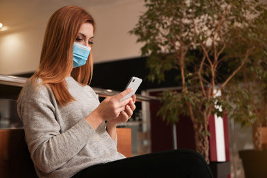 Photo of Woman with medical mask and mobile phone indoors. Virus protection