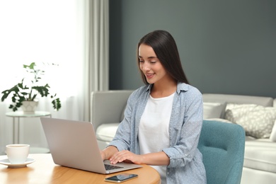 Photo of Young woman using laptop for search at wooden table in living room