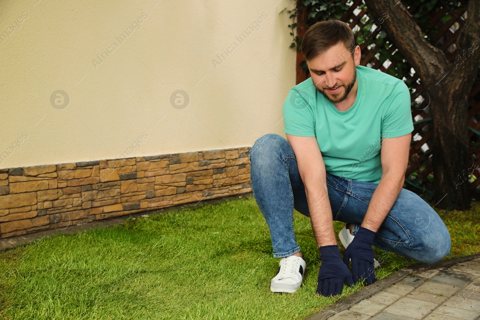 Photo of Young man laying grass sod at backyard, space for text