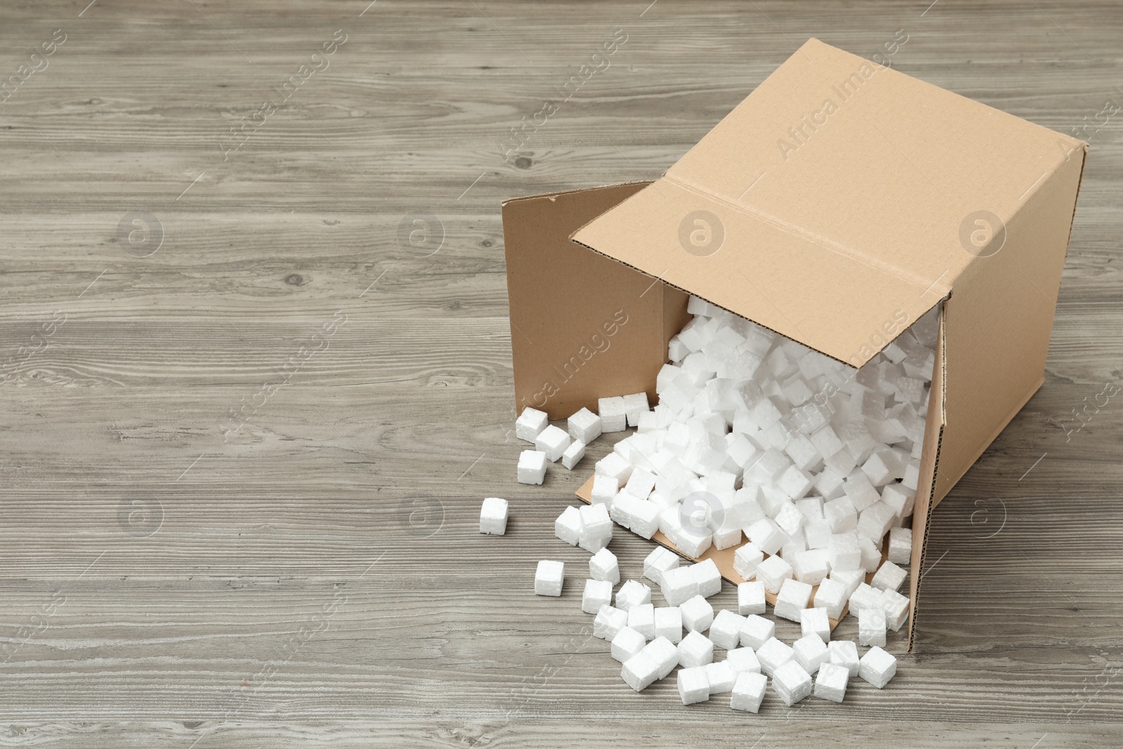 Photo of Overturned cardboard box with styrofoam cubes on wooden floor. Space for text