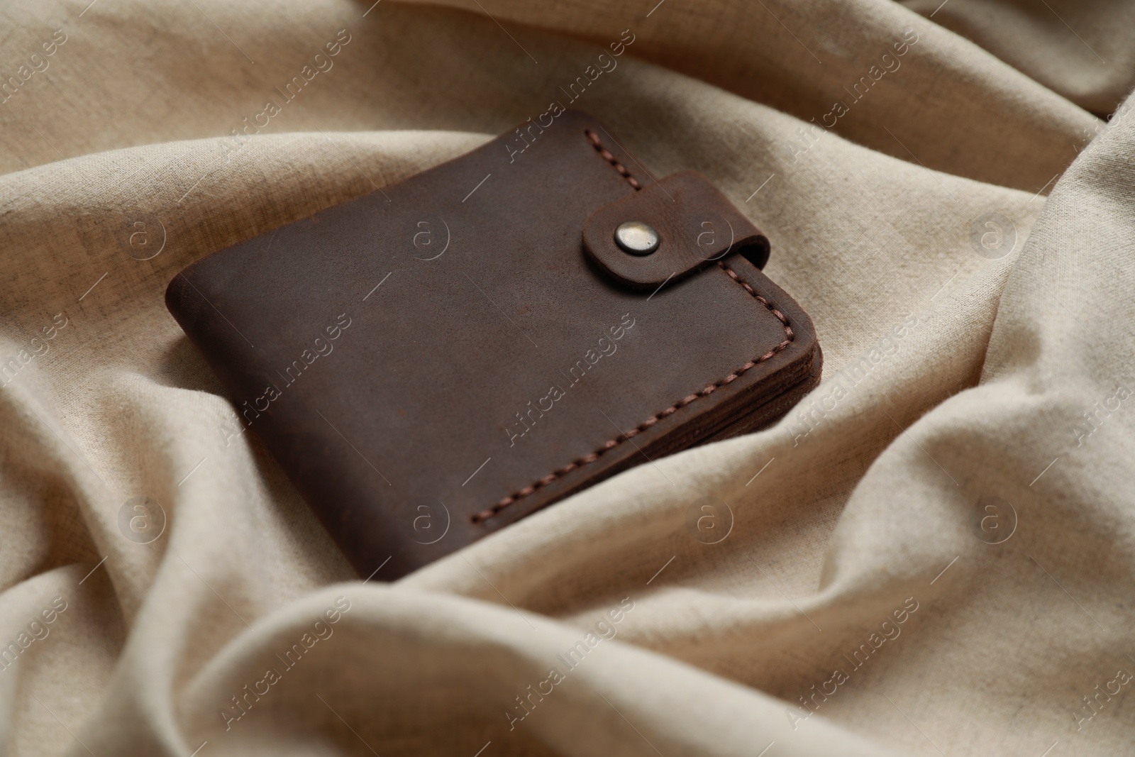 Photo of Stylish presentation of leather wallet on beige fabric, closeup