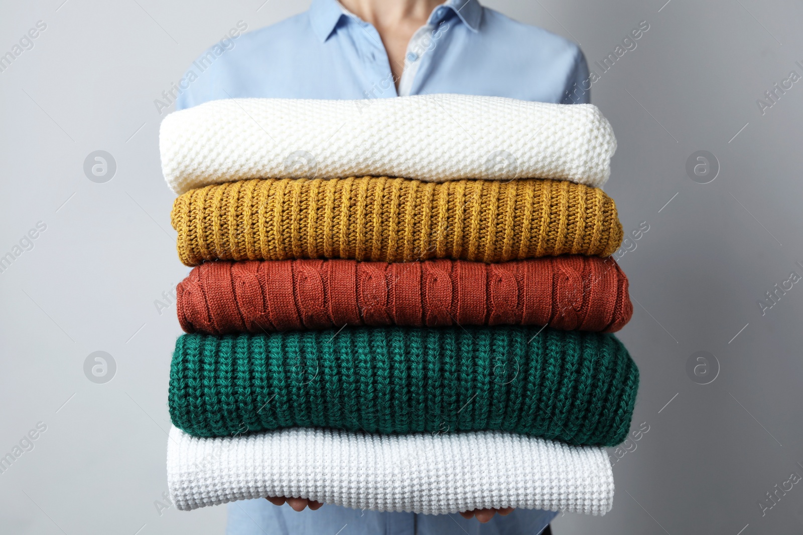 Photo of Woman holding stack of warm clothes on grey background, closeup. Autumn season