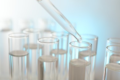 Photo of Dripping liquid from pipette into test tube on light background, closeup