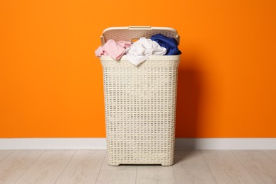 Photo of Laundry basket with clothes near orange wall indoors