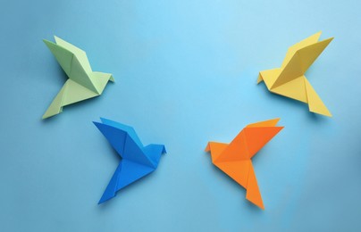 Photo of Origami art. Colorful handmade paper birds on light blue background, flat lay. Space for text