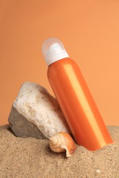 Sand with bottle of sunscreen, stone and seashell against orange background. Sun protection