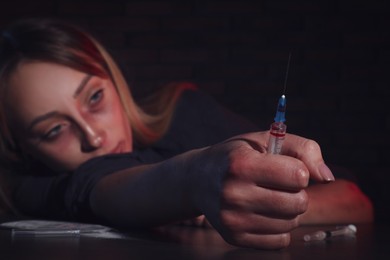 Photo of Drug addicted woman with syringe at table, focus on hand
