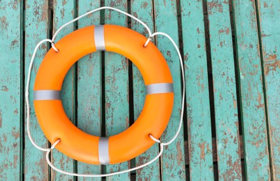 Orange life buoy on turquoise wooden background, top view. Space for text