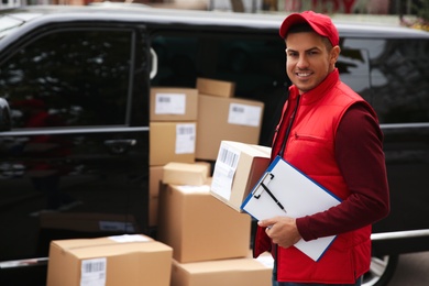 Courier with clipboard near delivery van outdoors. Space for text
