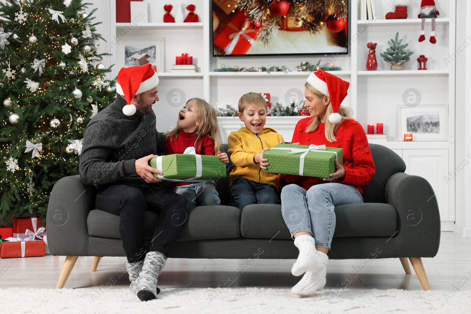 Photo of Happy family in Santa hats with Christmas gifts on sofa at home