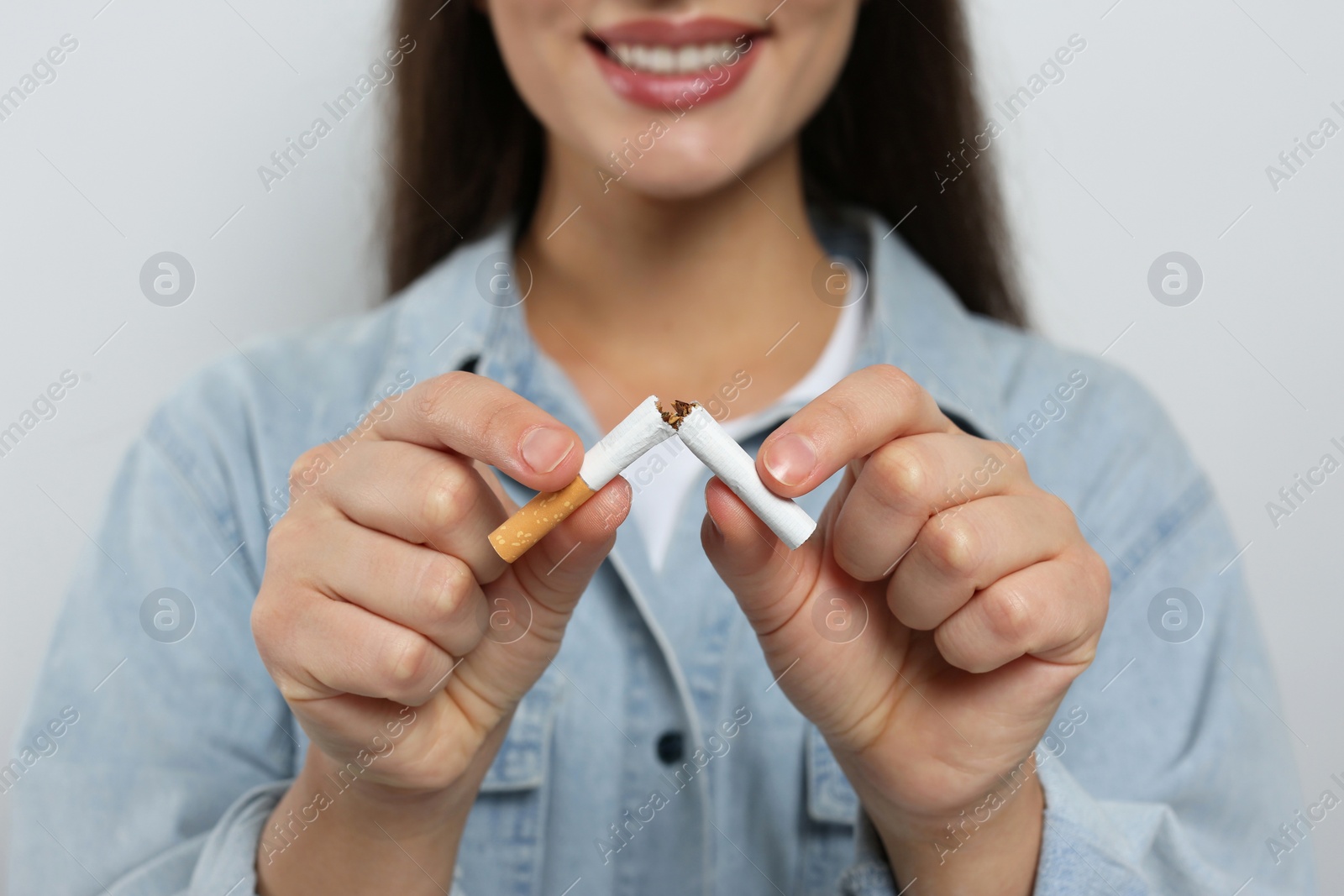 Photo of Stop smoking concept. Woman breaking cigarette on light grey background, closeup