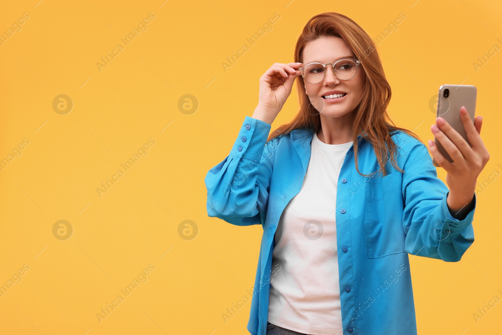 Photo of Beautiful woman in eyeglasses taking selfie on orange background. Space for text