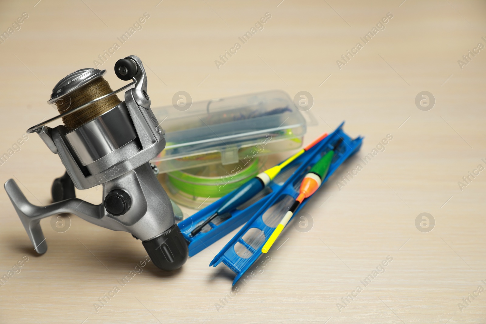 Photo of Reel with fishing line, baits and floats on light wooden table, closeup. Space for text