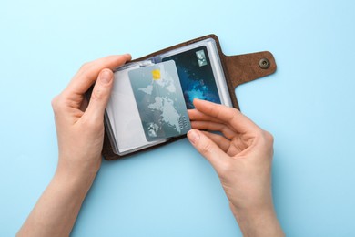 Photo of Woman holding leather card holder with credit cards on light blue background, top view