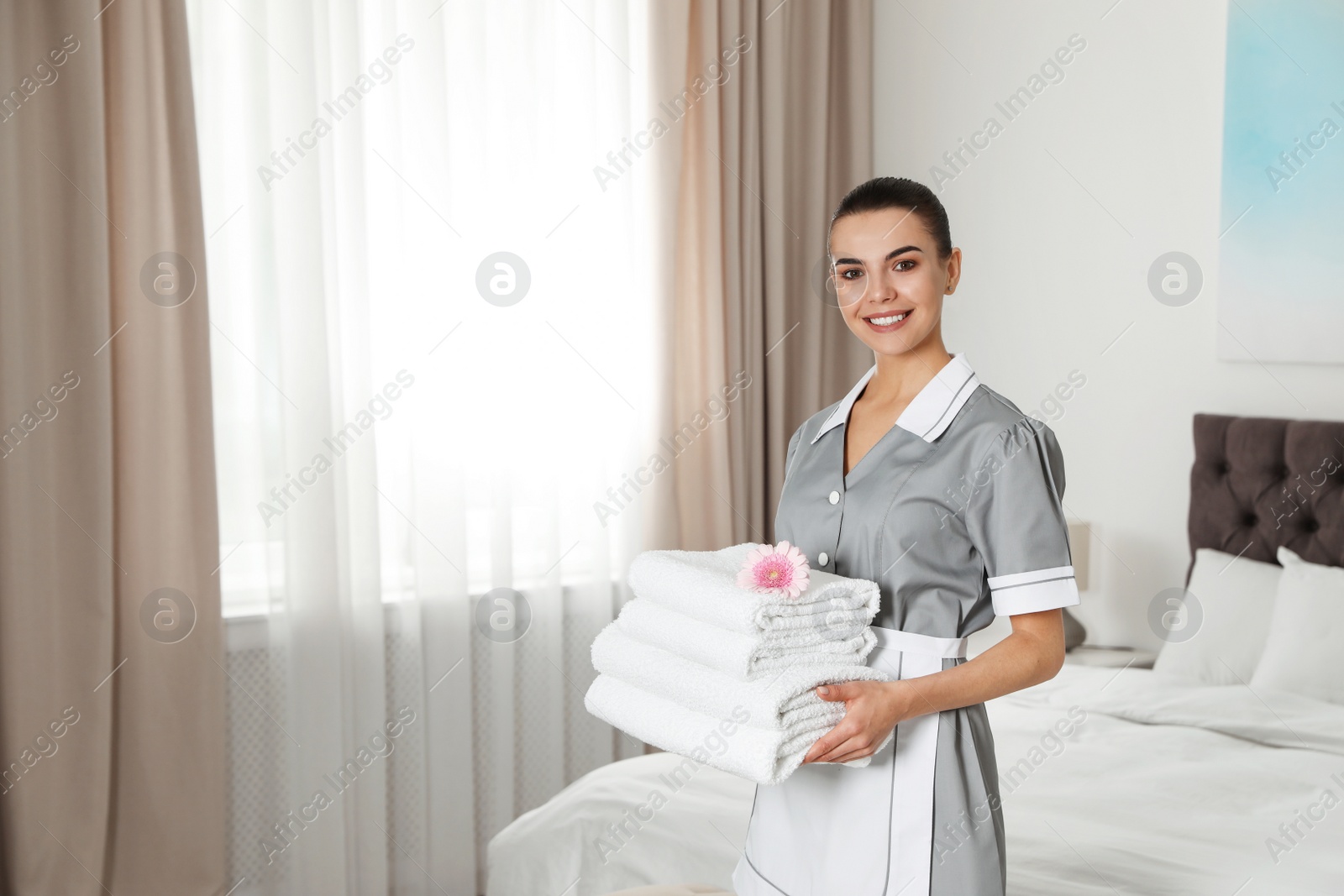 Photo of Chambermaid with stack of fresh towels in hotel room. Space for text