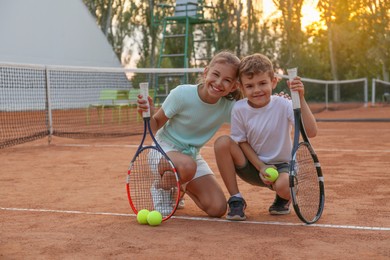 Photo of Cute children with tennis rackets and balls on court outdoors