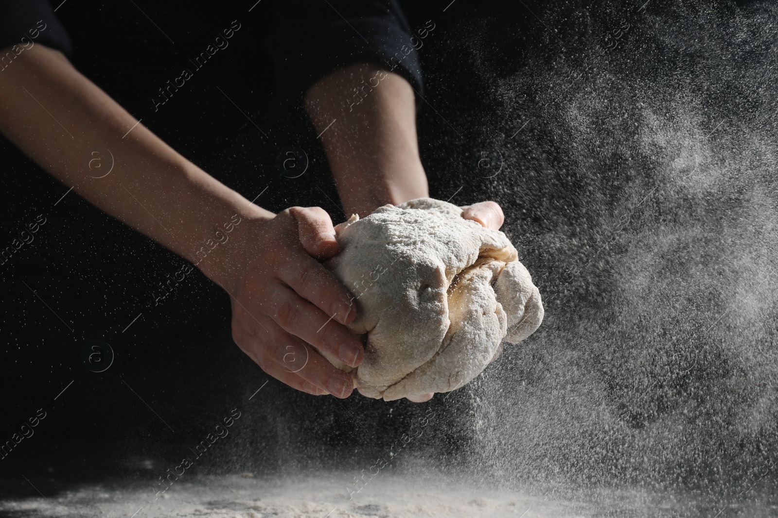 Photo of Making bread. Woman kneading dough at table on dark background, closeup