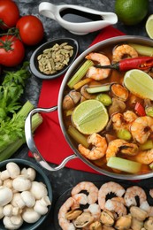 Saucepan with delicious Tom Yum soup and ingredients on black marble table, flat lay