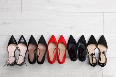 Photo of Red shoes among black ones on light wooden floor, flat lay. Diversity concept