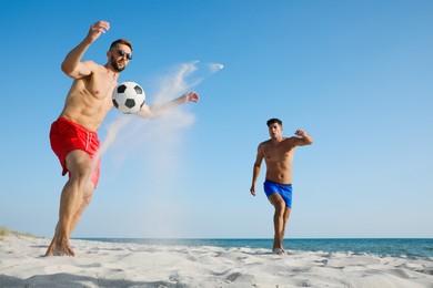 Friends playing football on sandy beach near sea