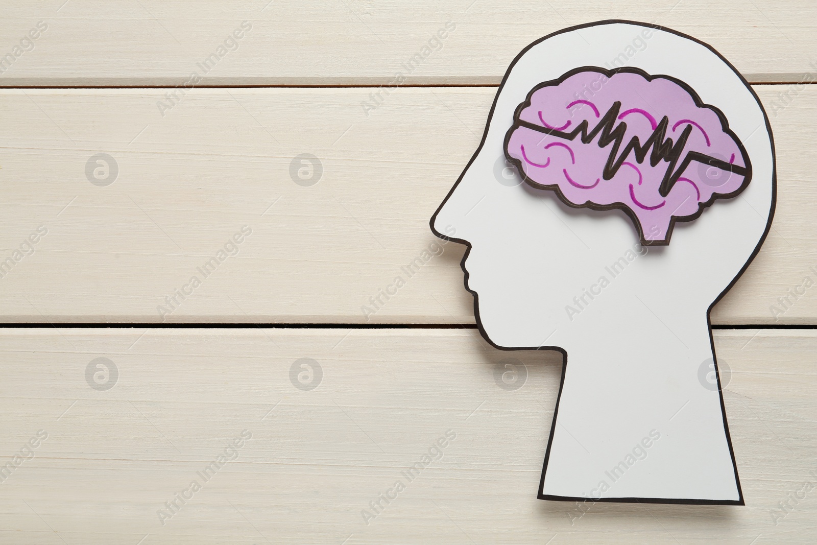 Photo of Top view of human head cutout with brain and pulse line on white wooden background, space for text. Epilepsy awareness