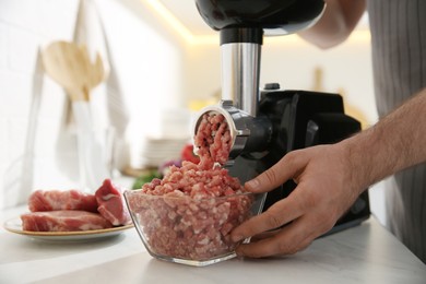 Photo of Man using modern meat grinder in kitchen, closeup