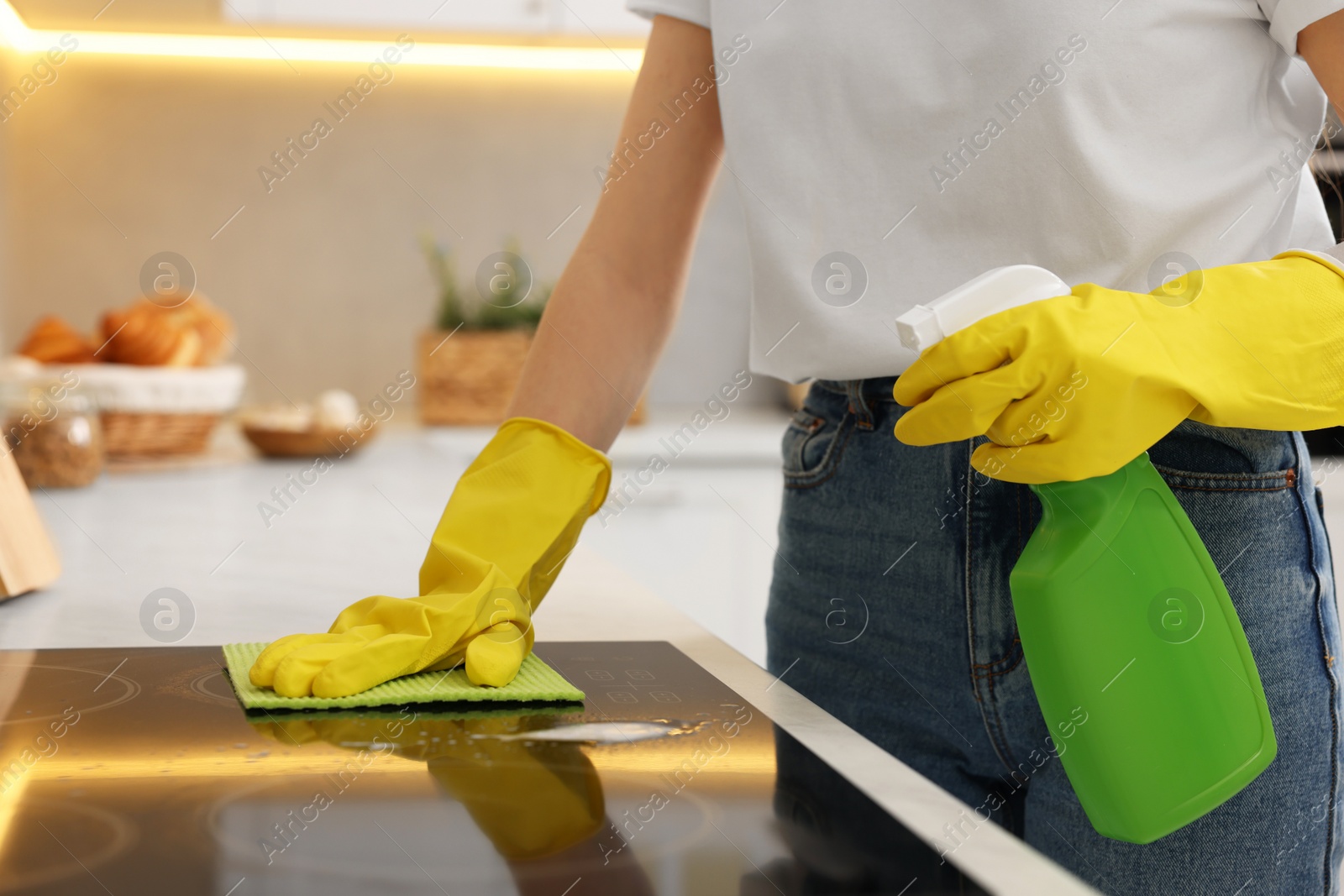 Photo of Woman with spray bottle and microfiber cloth cleaning electric stove in kitchen, closeup