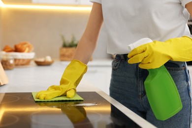 Photo of Woman with spray bottle and microfiber cloth cleaning electric stove in kitchen, closeup