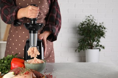 Woman making chicken mince with electric meat grinder at grey marble table indoors, closeup. Space for text