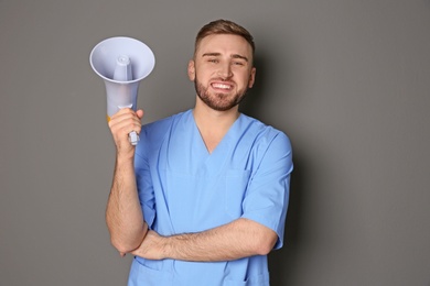 Male doctor with megaphone on grey background