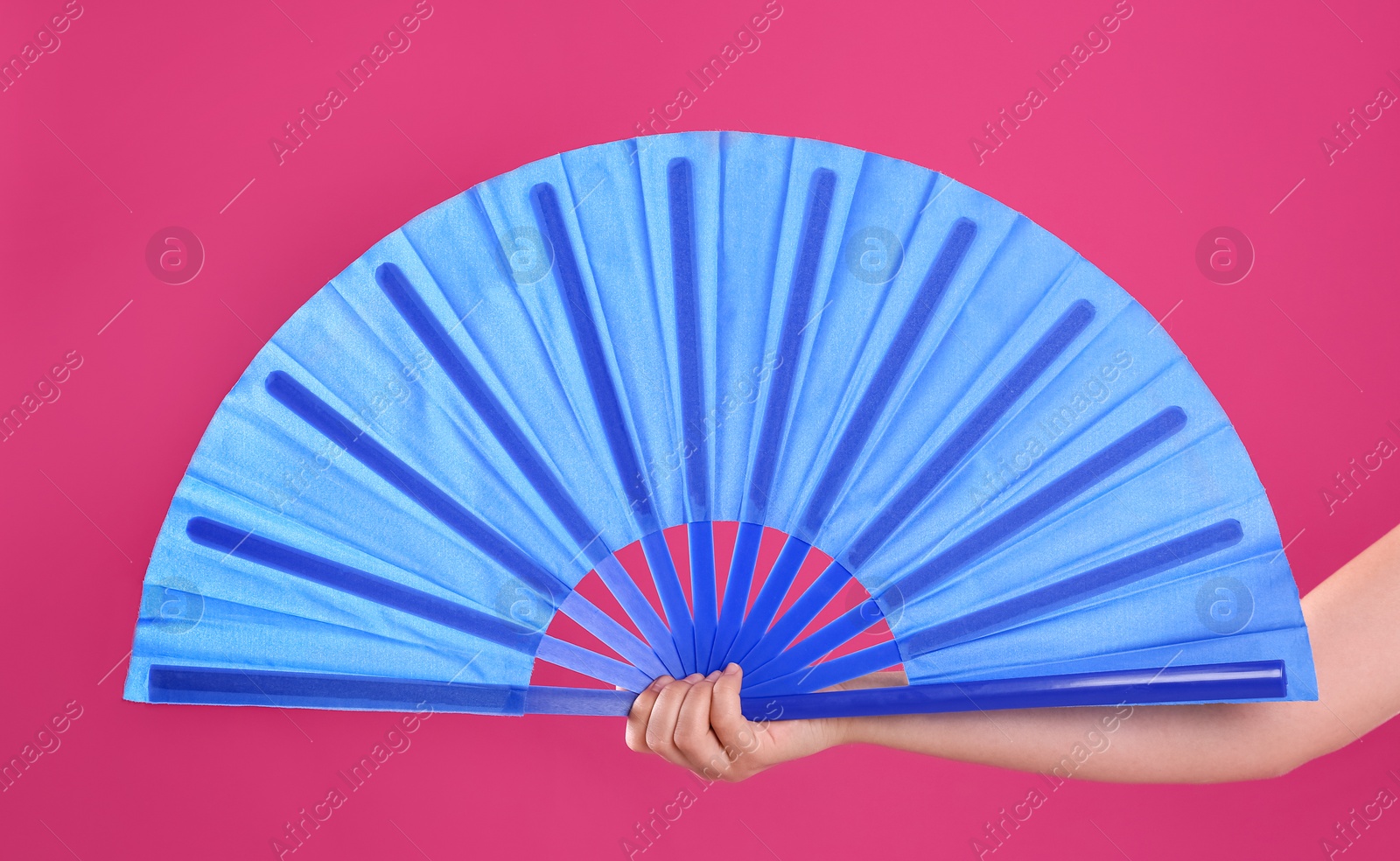 Photo of Woman holding blue hand fan on pink background, closeup