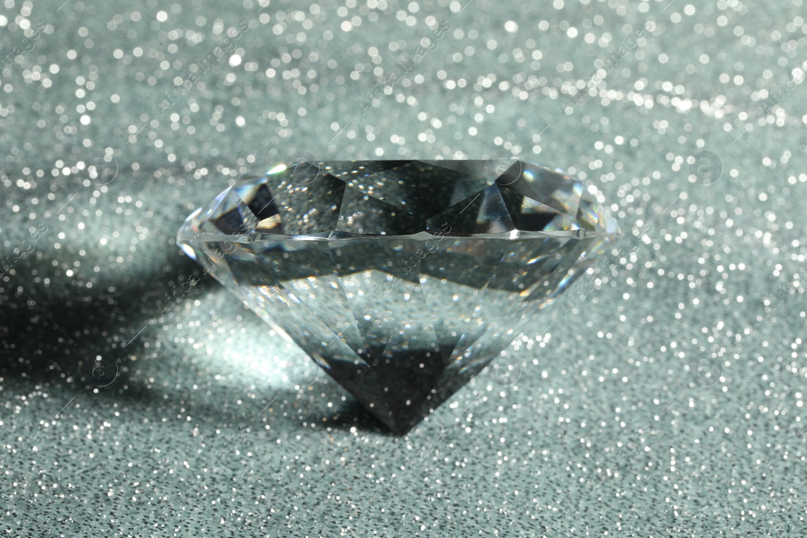Photo of Beautiful dazzling diamond on silver glitter background, closeup