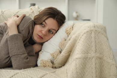 Sad young woman lying on sofa at home, space for text