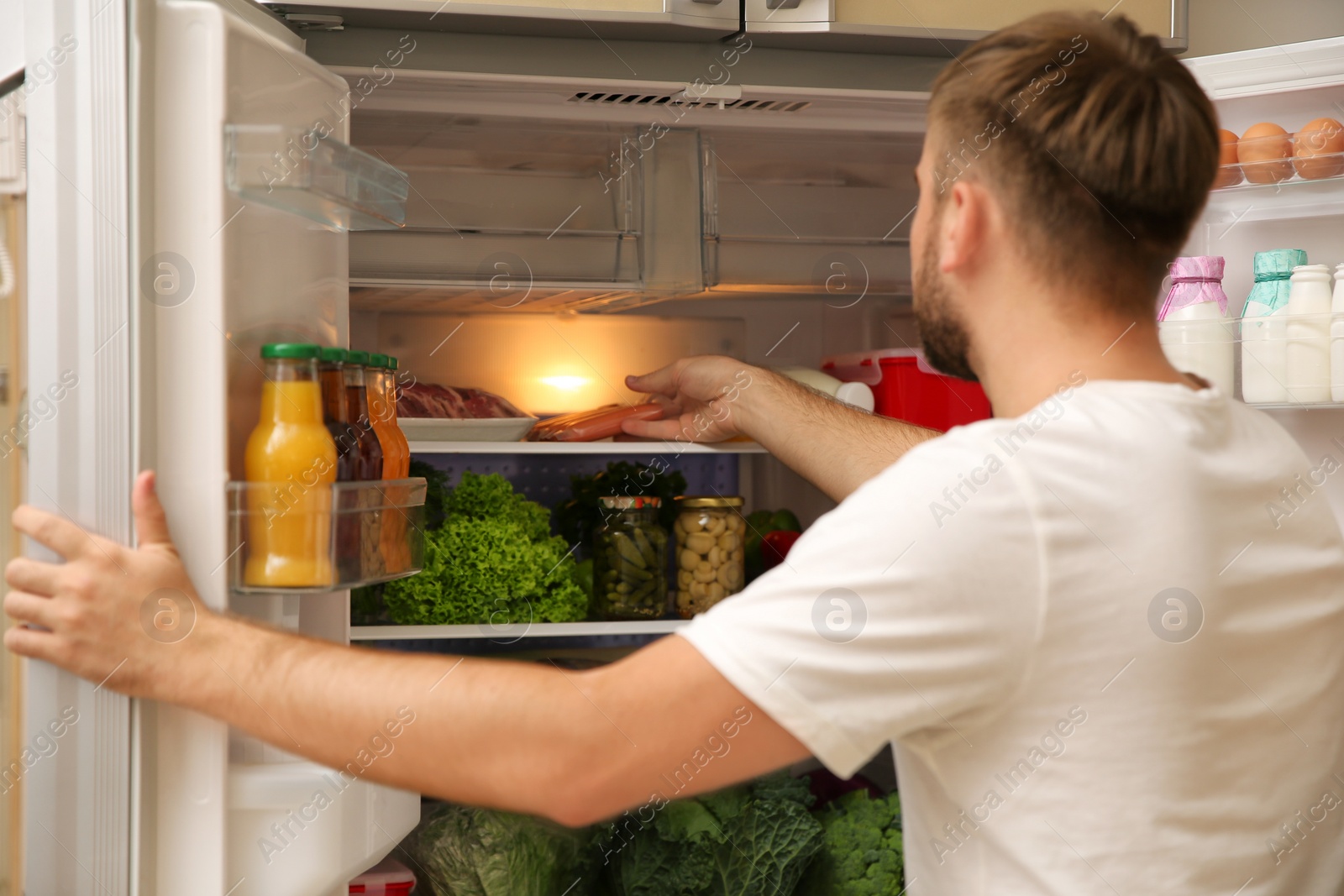 Photo of Young man taking sausages from refrigerator in kitchen