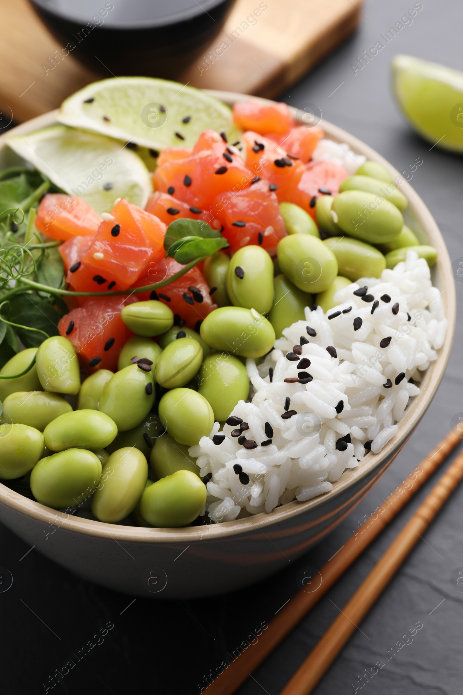 Photo of Delicious poke bowl with lime, fish and edamame beans on black table