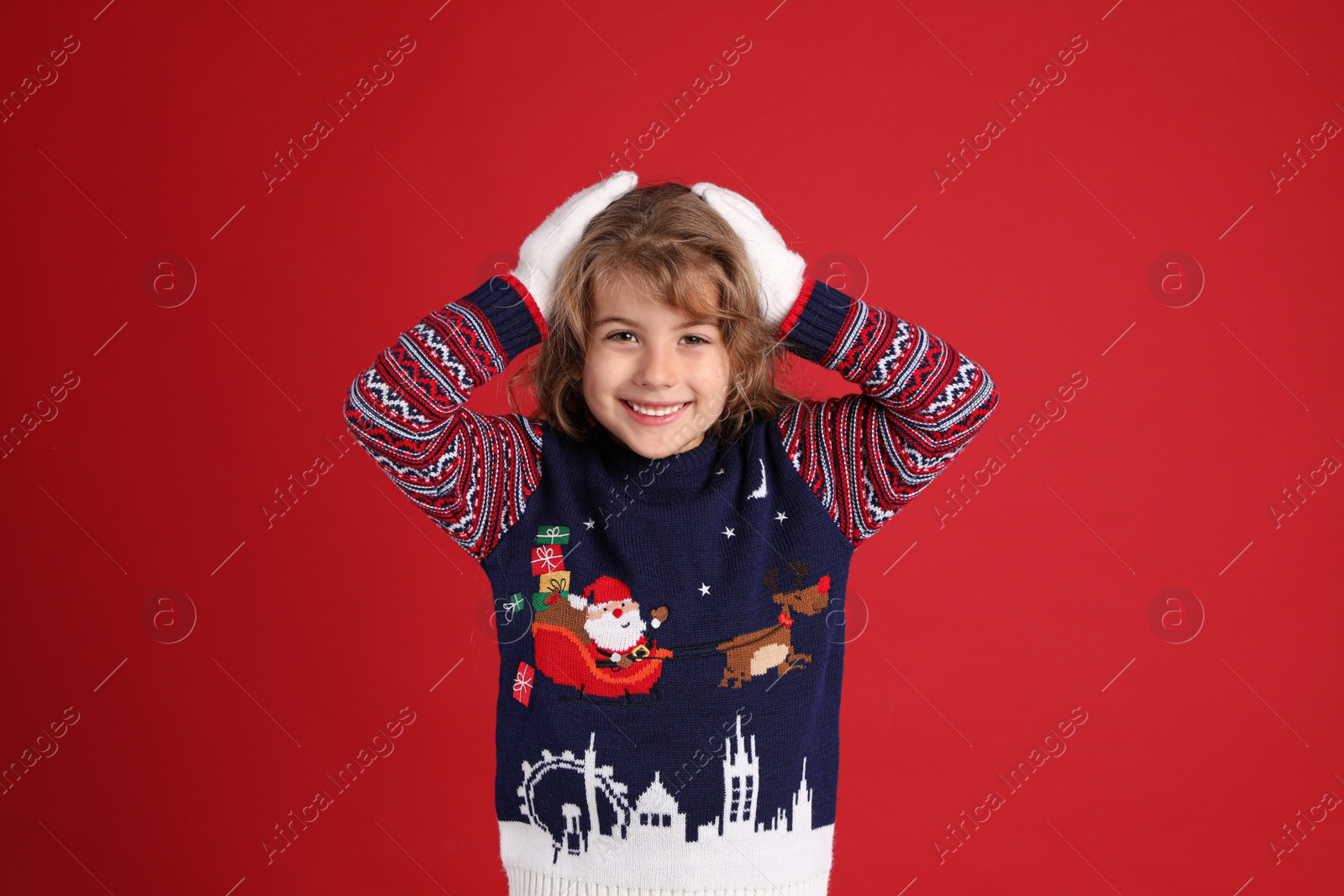 Photo of Cute little girl in Christmas sweater smiling against red background