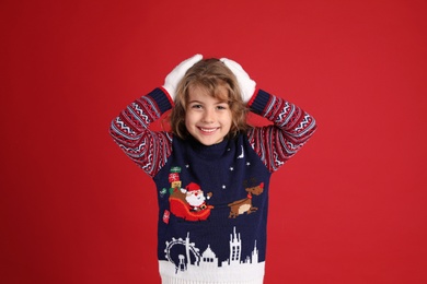 Photo of Cute little girl in Christmas sweater smiling against red background