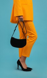 Young woman wearing stylish orange clothes with bag on light blue background, closeup