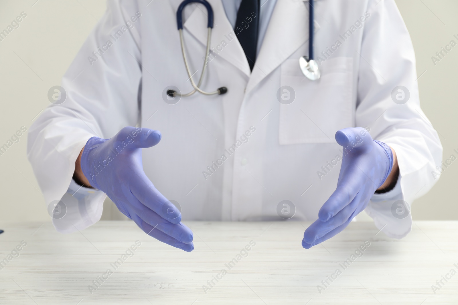 Photo of Doctor in gloves holding something at white table, closeup