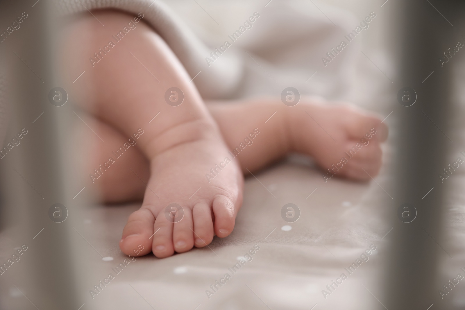 Photo of Cute little baby lying in crib, closeup of feet. Bedtime