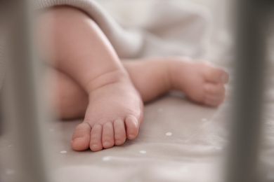 Cute little baby lying in crib, closeup of feet. Bedtime